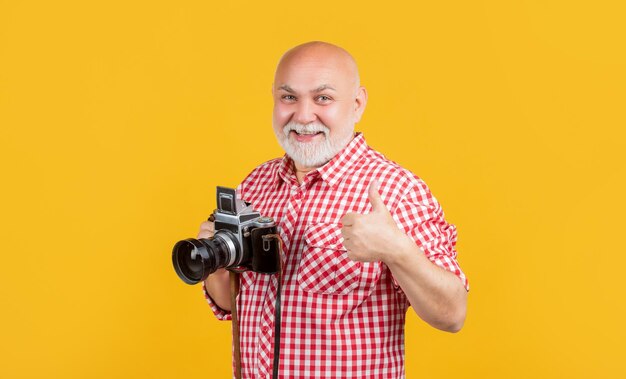 Homem envelhecido positivo com câmera fotográfica retrô no polegar de fundo amarelo para cima