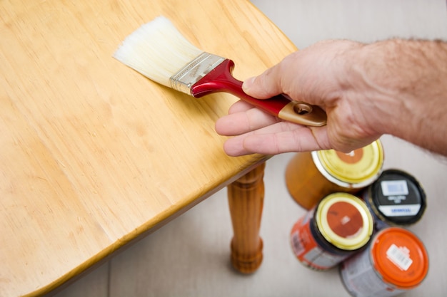 Homem envernizando uma cadeira com pincel