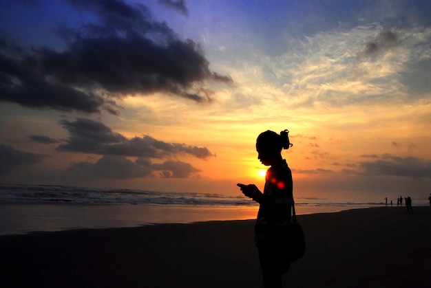 Homem enviando mensagens de texto usando smartphone na praia durante o pôr do sol