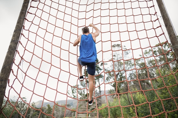 Homem escalando uma rede durante a pista de obstáculos no campo de treinamento