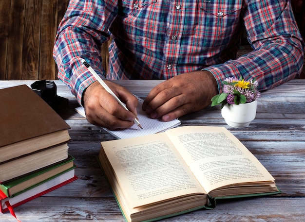 Foto homem escrevendo com caneta e lendo livros na mesa