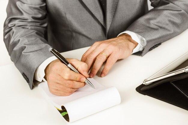 Homem escrevendo com uma caneta em um bloco de notas em uma mesa branca
