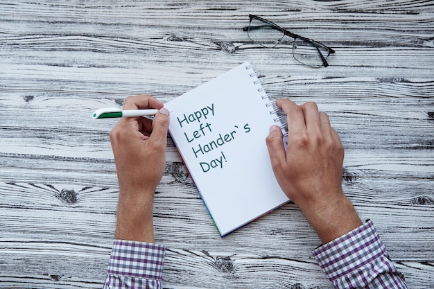 Foto homem escrevendo em um caderno feliz dia canhotos texto escreve com a mão esquerda em um bloco de notas