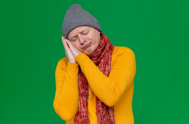 Homem eslavo adulto sonolento com chapéu de inverno e lenço no pescoço colocando a cabeça nas mãos