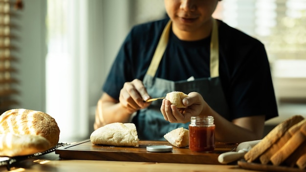 Homem espalhando doce geléia de framboesa no pão durante o café da manhã ou brunch na cozinha