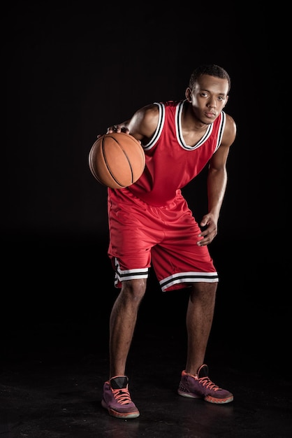 homem esportivo africano em uniforme esportivo jogando basquete em preto