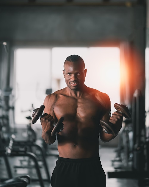 Homem esportivo africano usando exercícios com halteres no ginásio Musculação asiática para treinamento muscular Conceito de ginásio de saúde esportiva