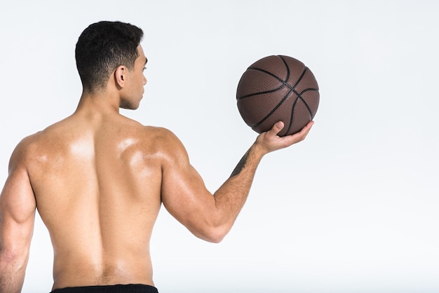 Homem esportivo de raça mista com torso musculoso segurando bola marrom em branco