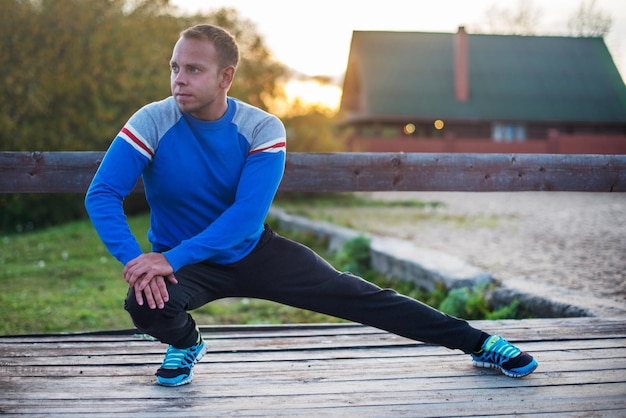 Homem esportivo esticando ao ar livre fazendo exercícios à noite ao pôr do sol conceitos de fitness