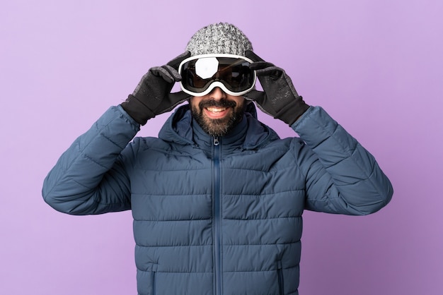 Homem esquiador com óculos de snowboard na parede roxa isolada