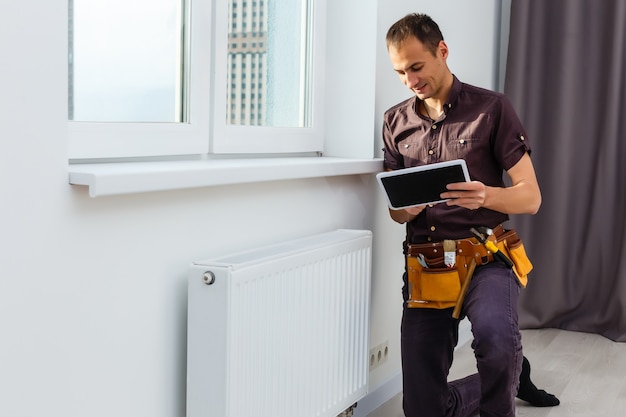 Homem está consertando a bateria do radiador na sala. reparação de manutenção obras de renovação no apartamento. recuperação de aquecimento. chave em mãos