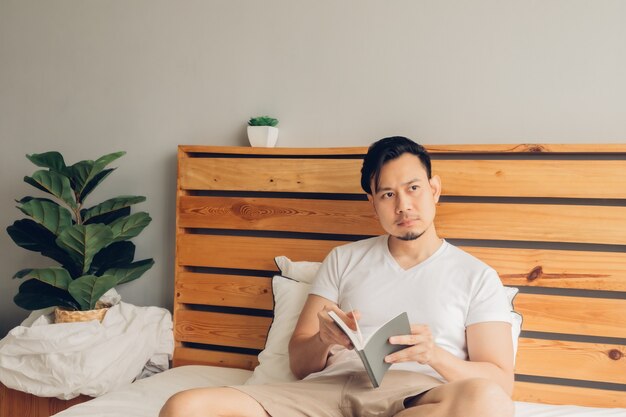 Homem está lendo um livro em sua cama no final da tarde.