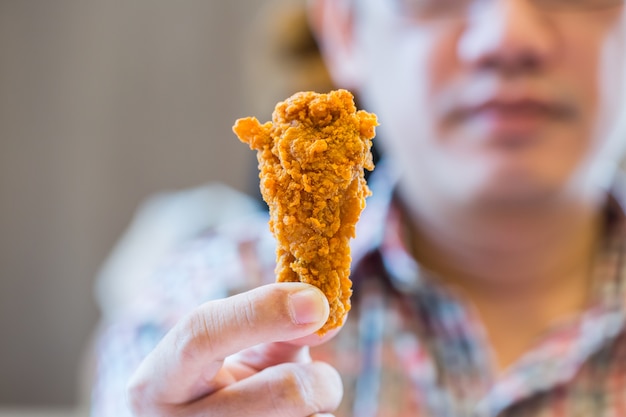 Homem está segurando a coxa de frango frito com fundo bure