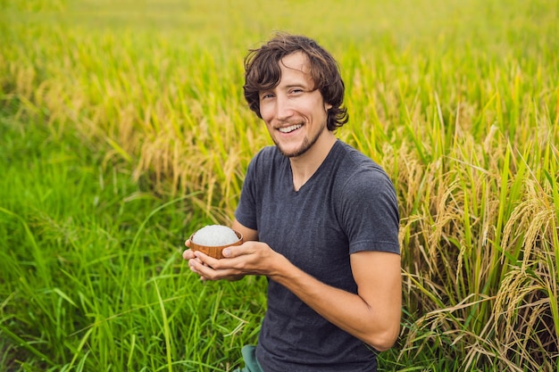 Homem está segurando uma xícara de arroz cozido em um copo de madeira no fundo de um campo de arroz maduro.