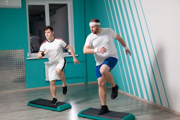 homem está trabalhando duro fazendo exercícios de step-up em etapas durante aulas de fitness em grupo