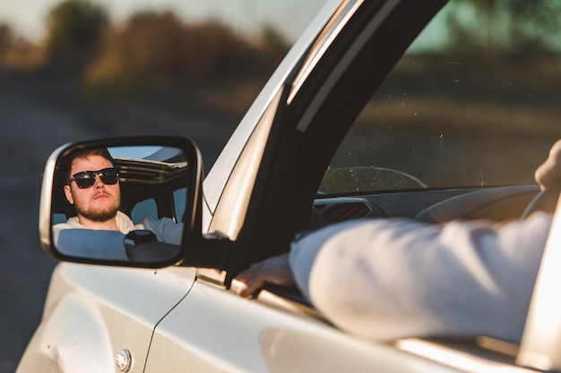 Homem estende a mão da janela do carro relaxado desfrutando ao pôr do sol