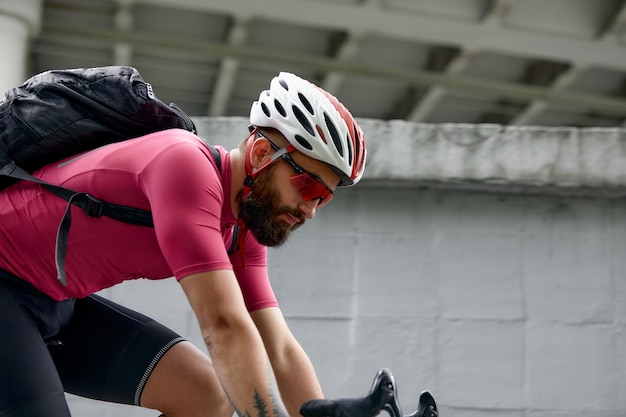 Homem estiloso andando pela cidade em bicicletas em um fim de semana andando em um fundo de uma parede cinza Foto minimalista de ciclista em um fundo de uma parede cinza