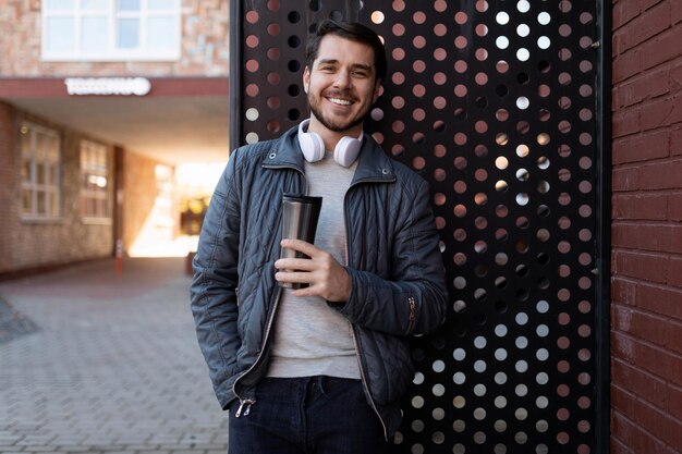 Homem estiloso anos de idade em fones de ouvido com um copo de café olhando para a câmera na rua