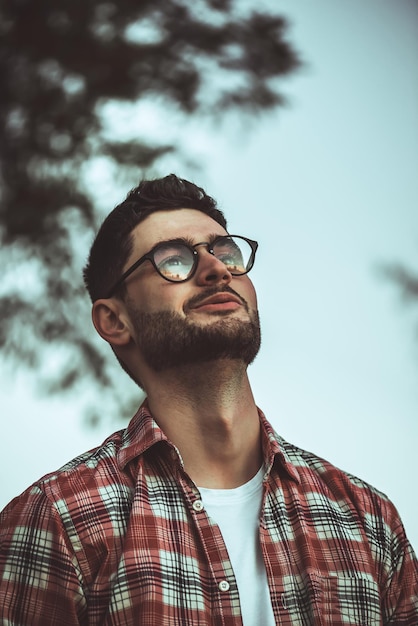 Homem estiloso, com barba e óculos escuros em pé no parque.