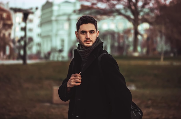 Homem estiloso, com barba e óculos escuros em pé no parque.