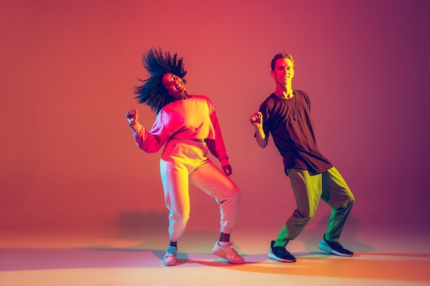 Foto homem estiloso e mulher dançando hip-hop em roupas brilhantes sobre fundo verde no salão de dança em luz de néon. cultura jovem, hip-hop, movimento, estilo e moda, ação. retrato elegante.