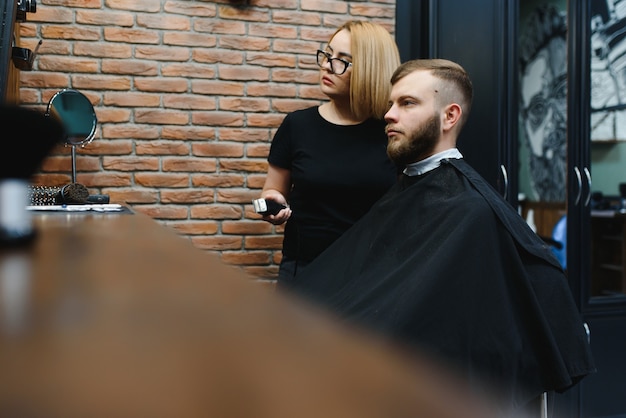 Homem estiloso sentado na barbearia Cabeleireiro Cabeleireiro Mulher cortando o cabelo dele