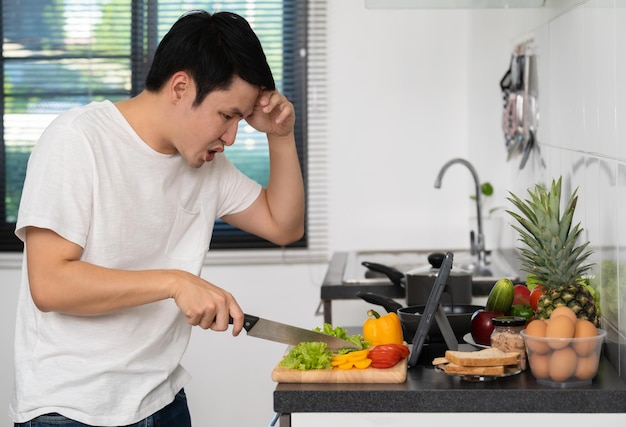 Homem estressado cozinhando e preparando legumes de acordo com uma receita em um tablet na cozinha em casa