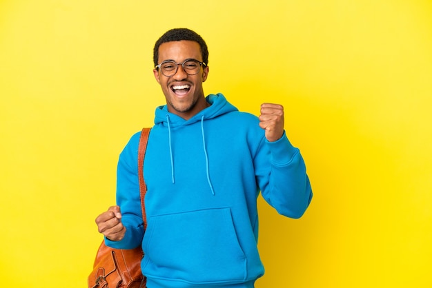 Homem estudante afro-americano sobre fundo amarelo isolado comemorando vitória