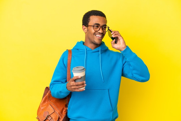 Homem estudante afro-americano sobre fundo amarelo isolado segurando um café para levar e um celular