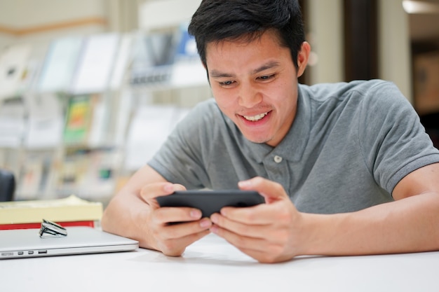 Homem estudante jogando jogo aplicação no smartphone após terminar de ler o livro