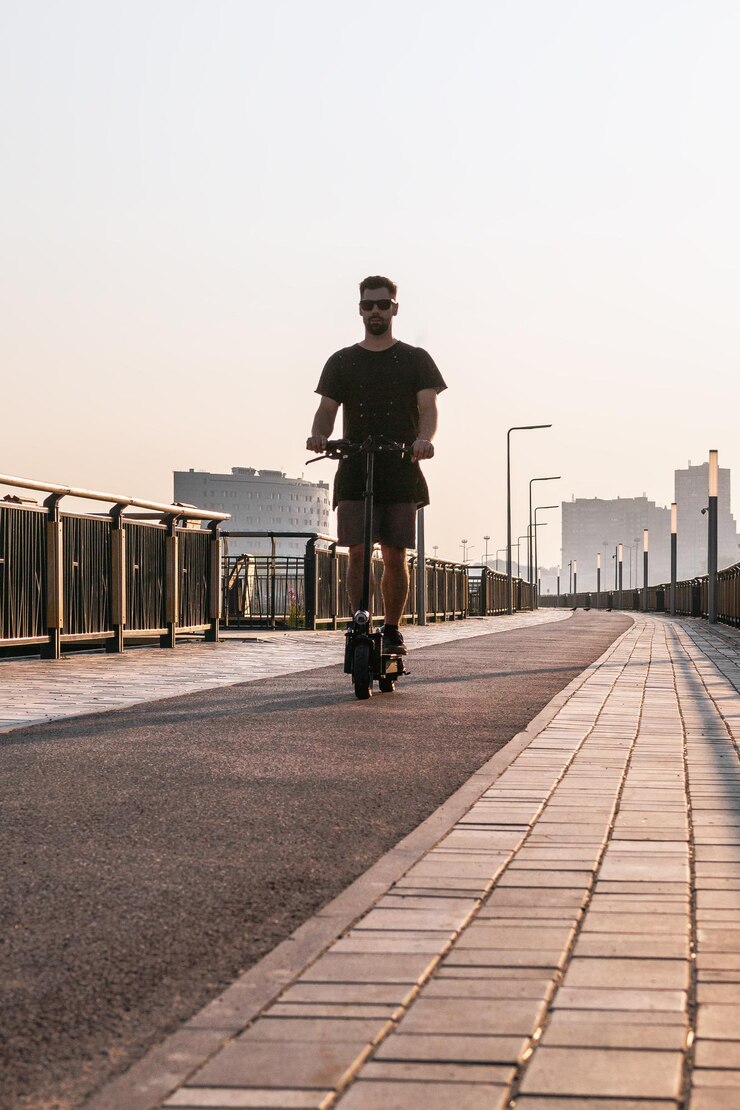 Foto homem europeu atraente está montado em uma scooter elétrica em uma rua vazia da cidade em um dia ensolarado