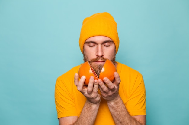 Homem europeu barbudo em camisa amarela isolado, cheirando a toranja deliciosa com os olhos fechados