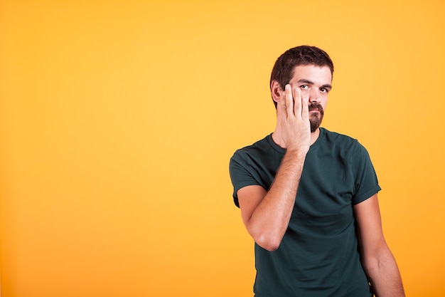 Foto homem expressivo estressado com as mãos no rosto em fundo laranja