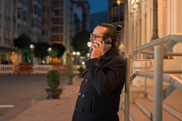 Homem fala ao telefone com as luzes da cidade ao fundo à noite