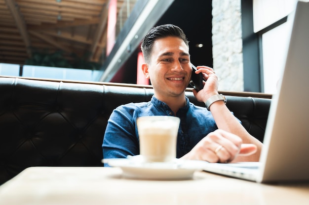 Homem falando no celular enquanto estiver usando o laptop do computador sentado na mesa de café