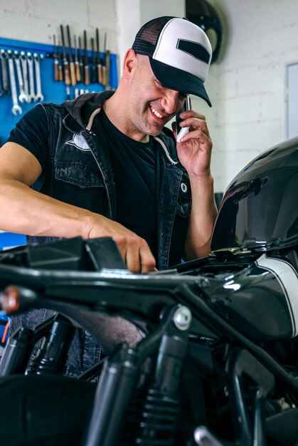 Foto homem falando no telefone móvel enquanto trabalha em motocicleta na garagem