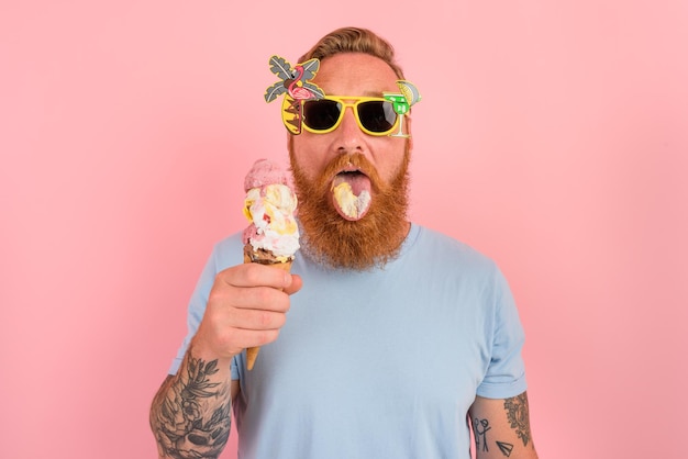 Homem faminto com barba e tatuagens comendo um grande sorvete