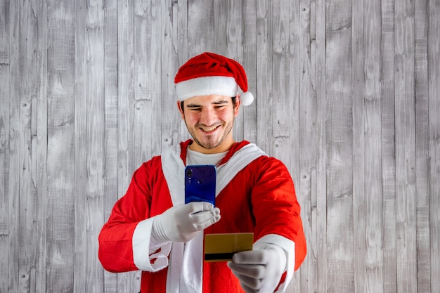 Homem fantasiado de Papai Noel com um celular e um cartão de crédito