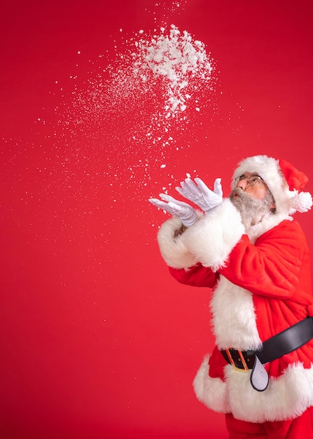 Homem fantasiado de papai noel soprando neve das mãos