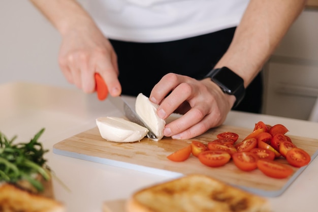 Homem fatia paz de mussarela na placa de madeira preparando sanduíche clássico italiano