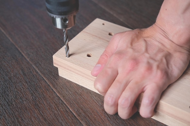 Homem faz furos na placa de madeira para produção de móveis artesanais em casa Móveis de montagem