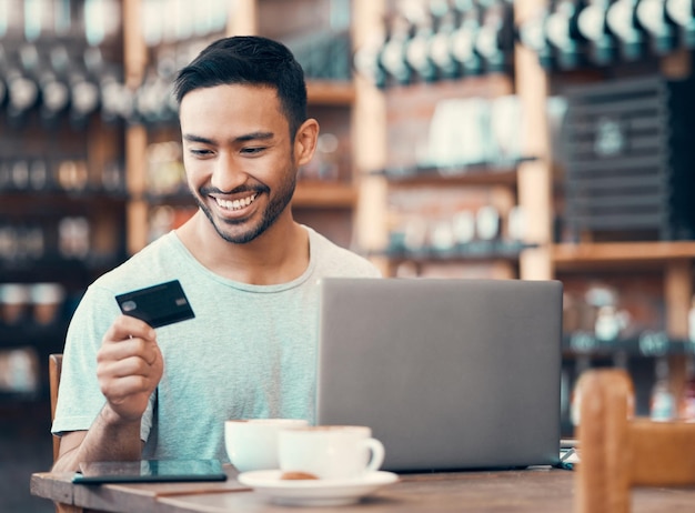 Homem fazendo compra ou empréstimo de compras on-line com cartão de crédito e laptop em um cibercafé Jovem homem feliz pagando dívida de seguro em um aplicativo bancário digital com tecnologia moderna e parecendo satisfeito