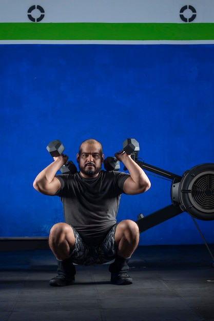 Foto homem fazendo exercícios com halteres na academia com fundo de cor azul