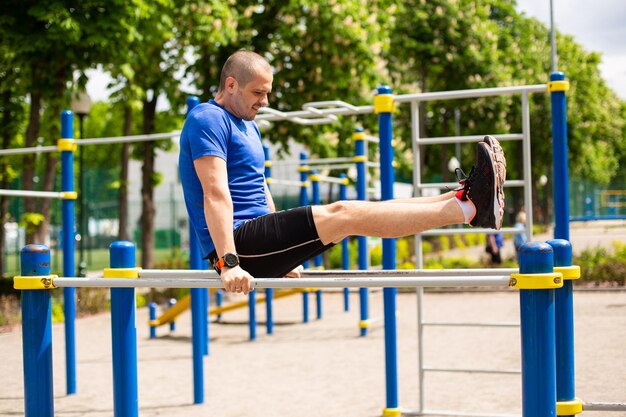 Homem fazendo exercícios em bares no campo de esportes no parque urbano de verão