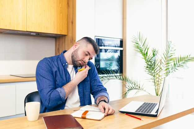 Homem fazendo negócios enquanto fica em casa sentado na cozinha à mesa e usando um laptop