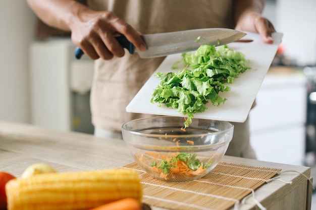 Homem fazendo salada e colocando alface depois de cortar em uma tigela na cozinha