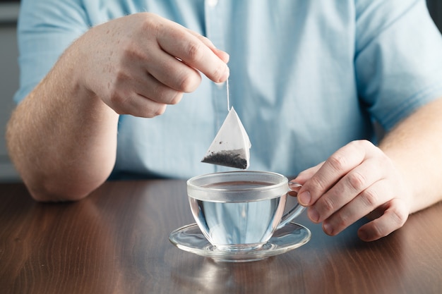 Homem fazendo saquinho de chá com copo de chá na mesa