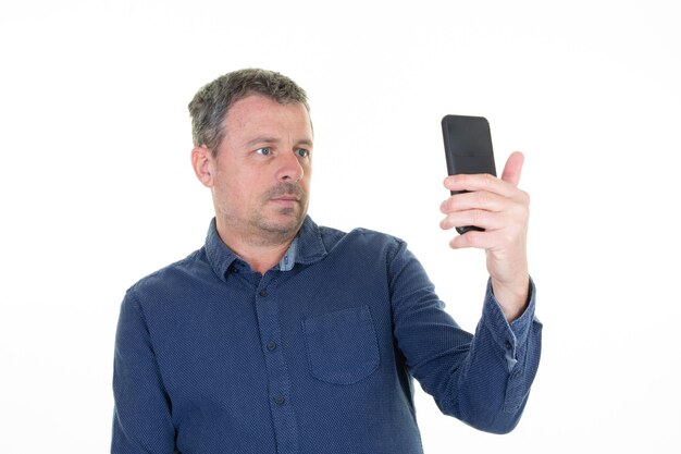 Homem fazendo selfie em smartphone com telefone celular em fundo branco. Retrato de cara bonito de meia-idade