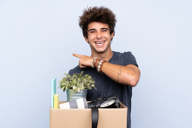 Homem fazendo um movimento ao pegar uma caixa cheia de coisas apontando o dedo para o lado