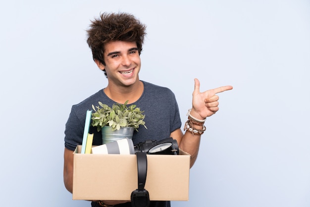 Homem fazendo um movimento ao pegar uma caixa cheia de coisas apontando o dedo para o lado